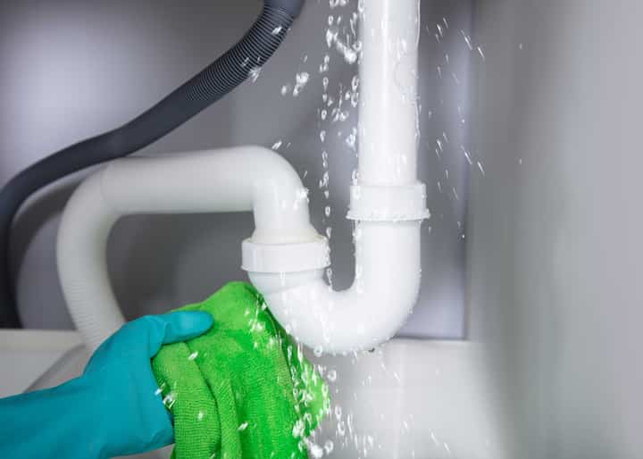 A gloved hand holding a rag trying to capture the water leaking from a pipe in Brooksville, FL